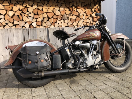 Kupferbraune Harley mit Ledersatteltasche und Solositz vor dem Holzunterstand